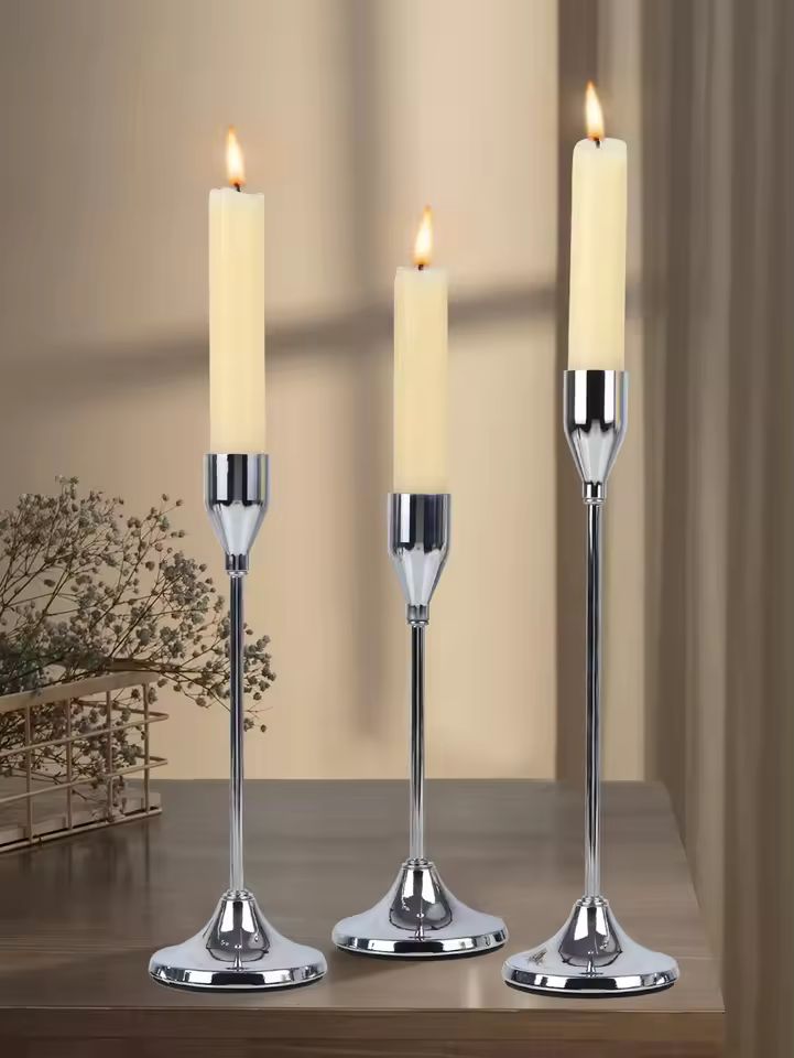 Silver Éclat candle holder set with three lit candles displayed on a wooden table in an elegant modern interior.