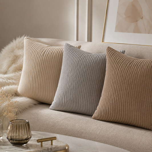 Minimalist velvet cushion covers in beige, grey and brown on a modern sofa.